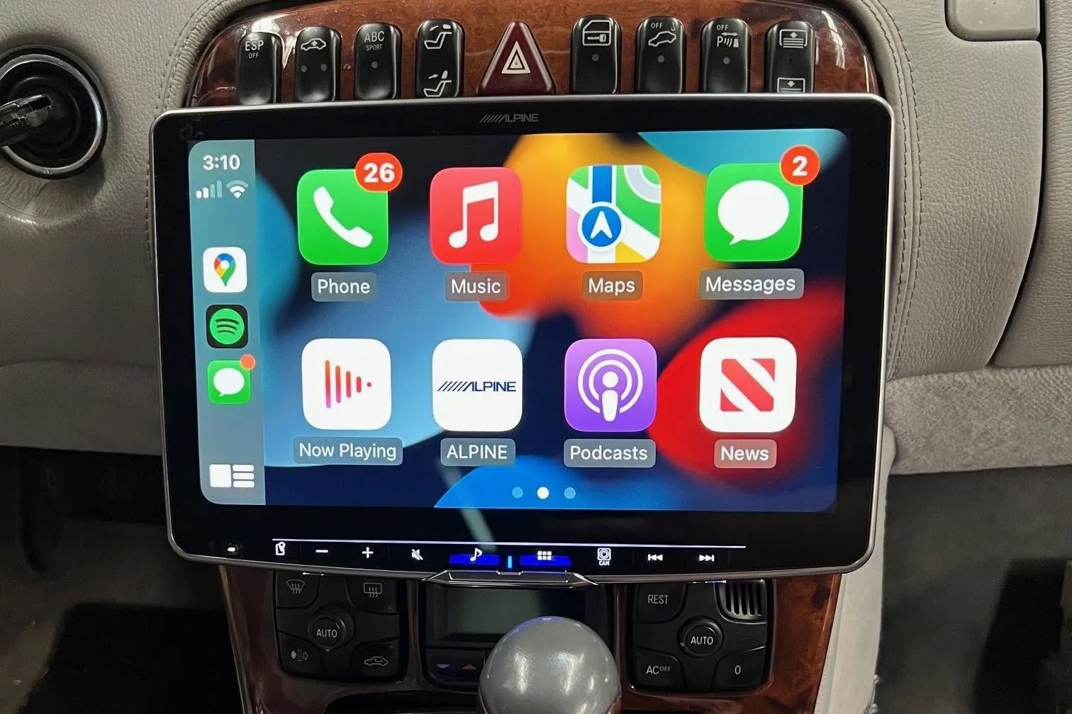 A car's dashboard with a modern touchscreen display showing Apple CarPlay apps, surrounded by wood and silver trim.
