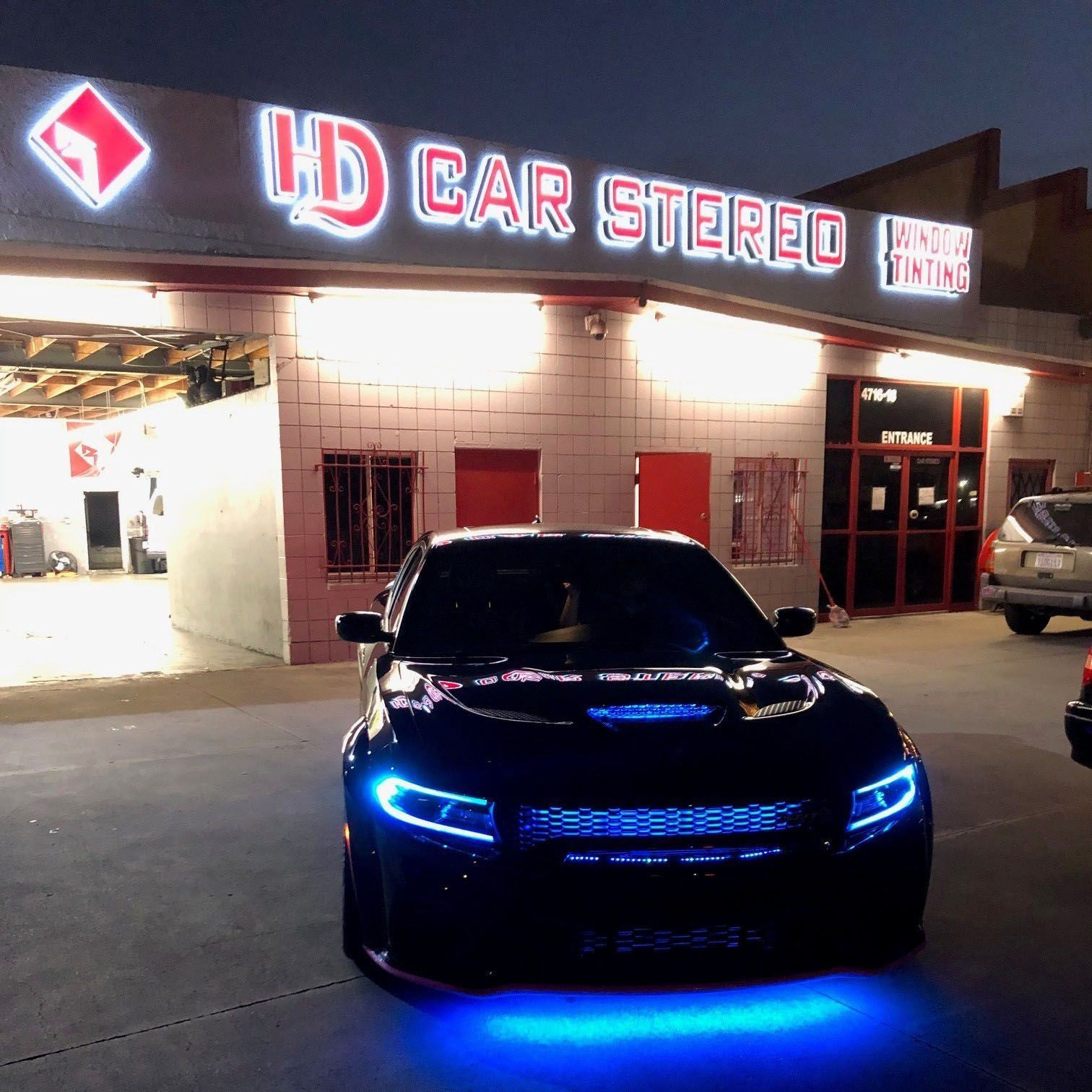 Black car with blue lights in front of HD Car Stereo shop at night.