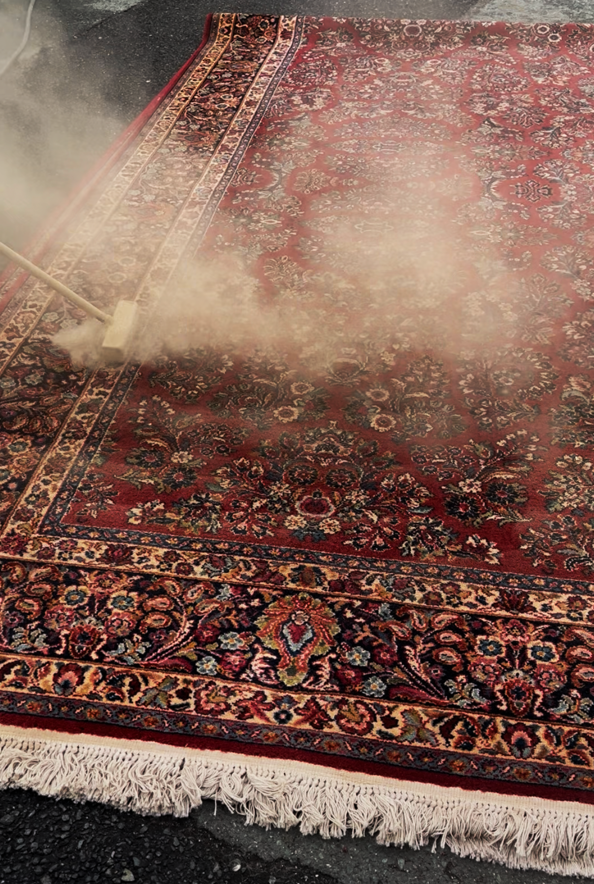 Red patterned carpet being cleaned with steam, covered in mist and dust in a workshop or cleaning area