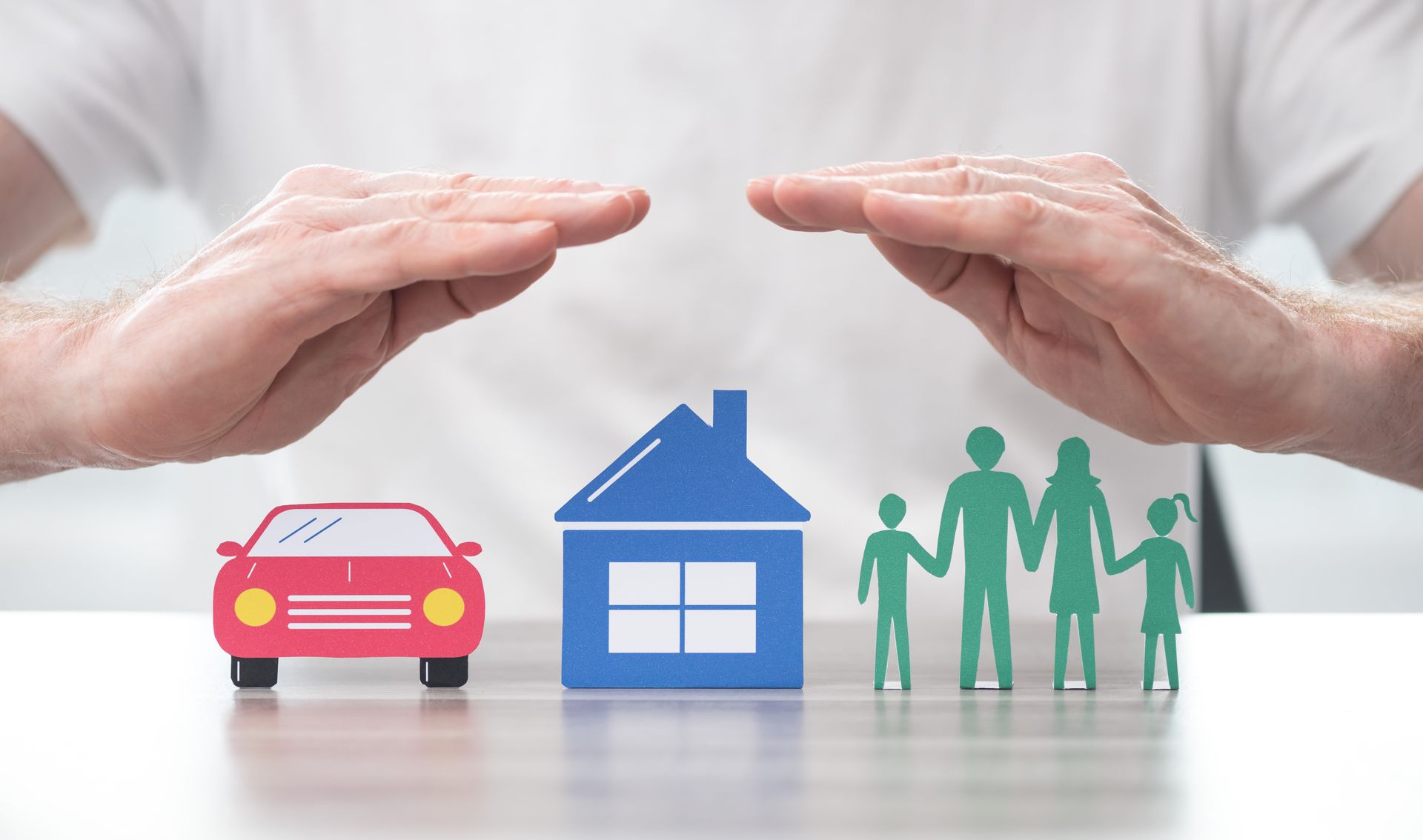 Hands protecting cut-out car, house, and family.