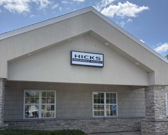 Front view of a building with beige stucco, stone base, and a sign under a blue sky