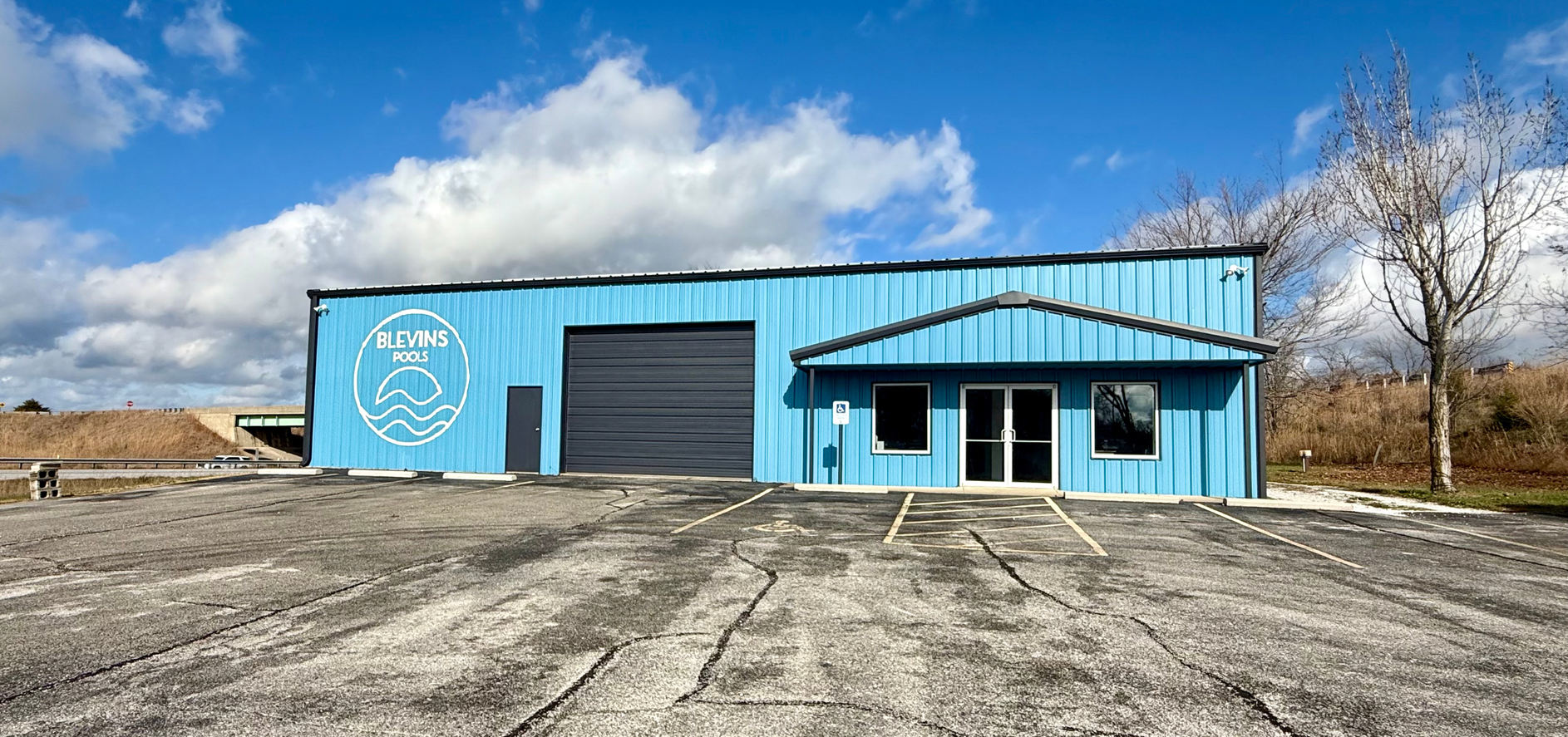 Blue building with logo, garage door, and entry door. Cloudy sky.
