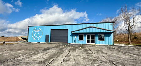 Blue building with logo, garage door, and entry door. Cloudy sky.