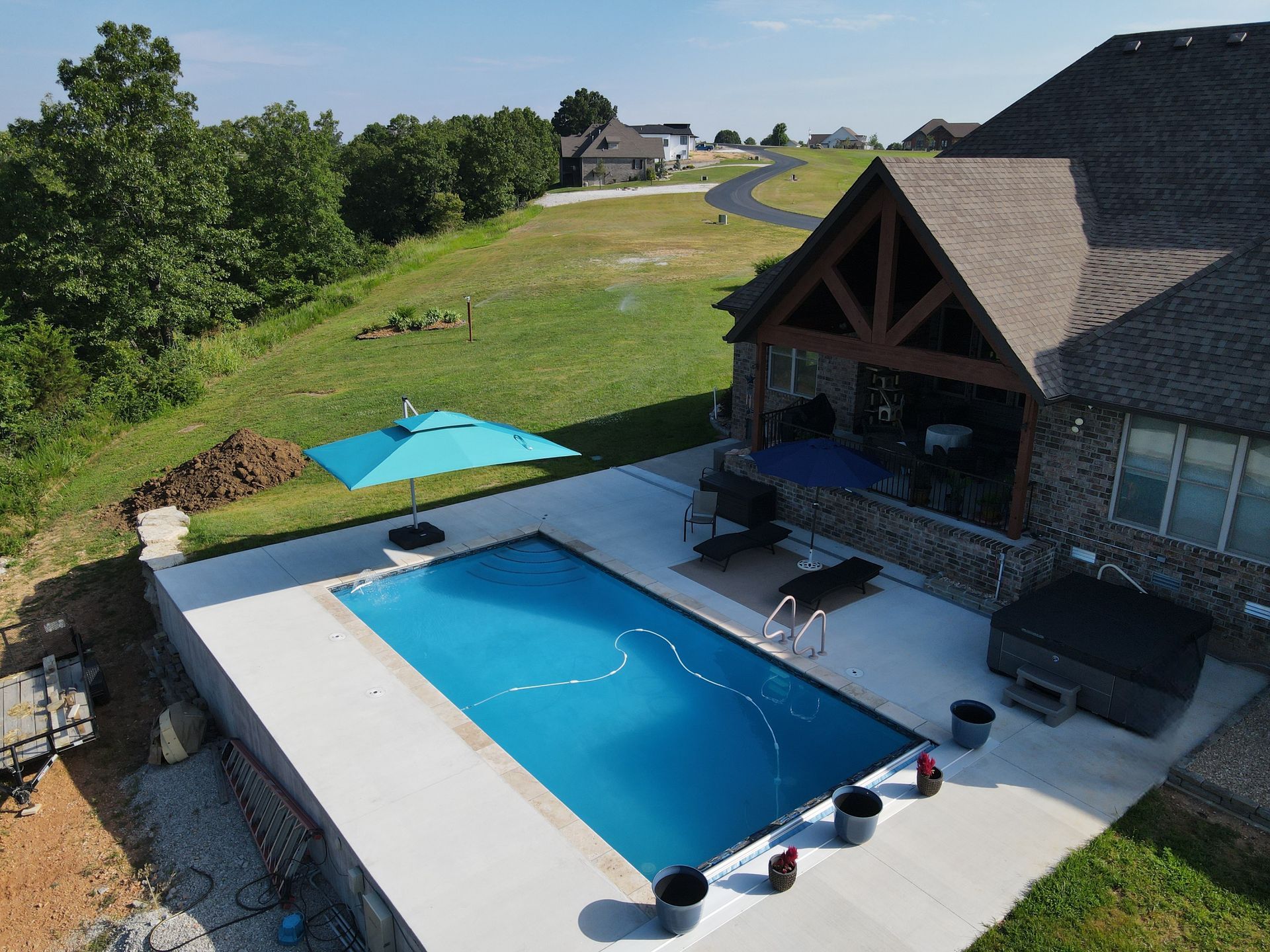 Pool and patio area with a house, umbrella, and a hot tub.