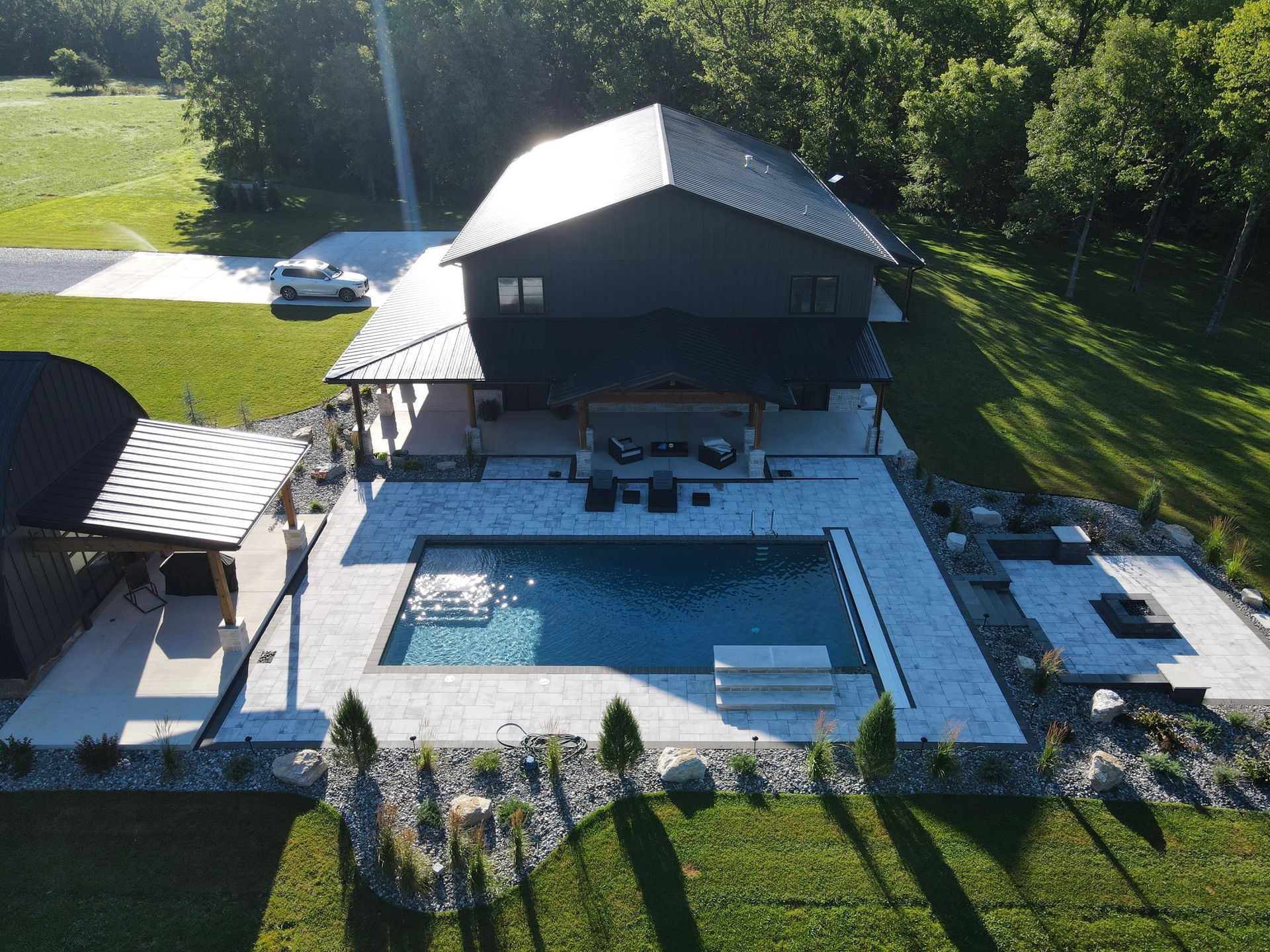 Aerial view of a modern black house with a pool and patio surrounded by greenery.
