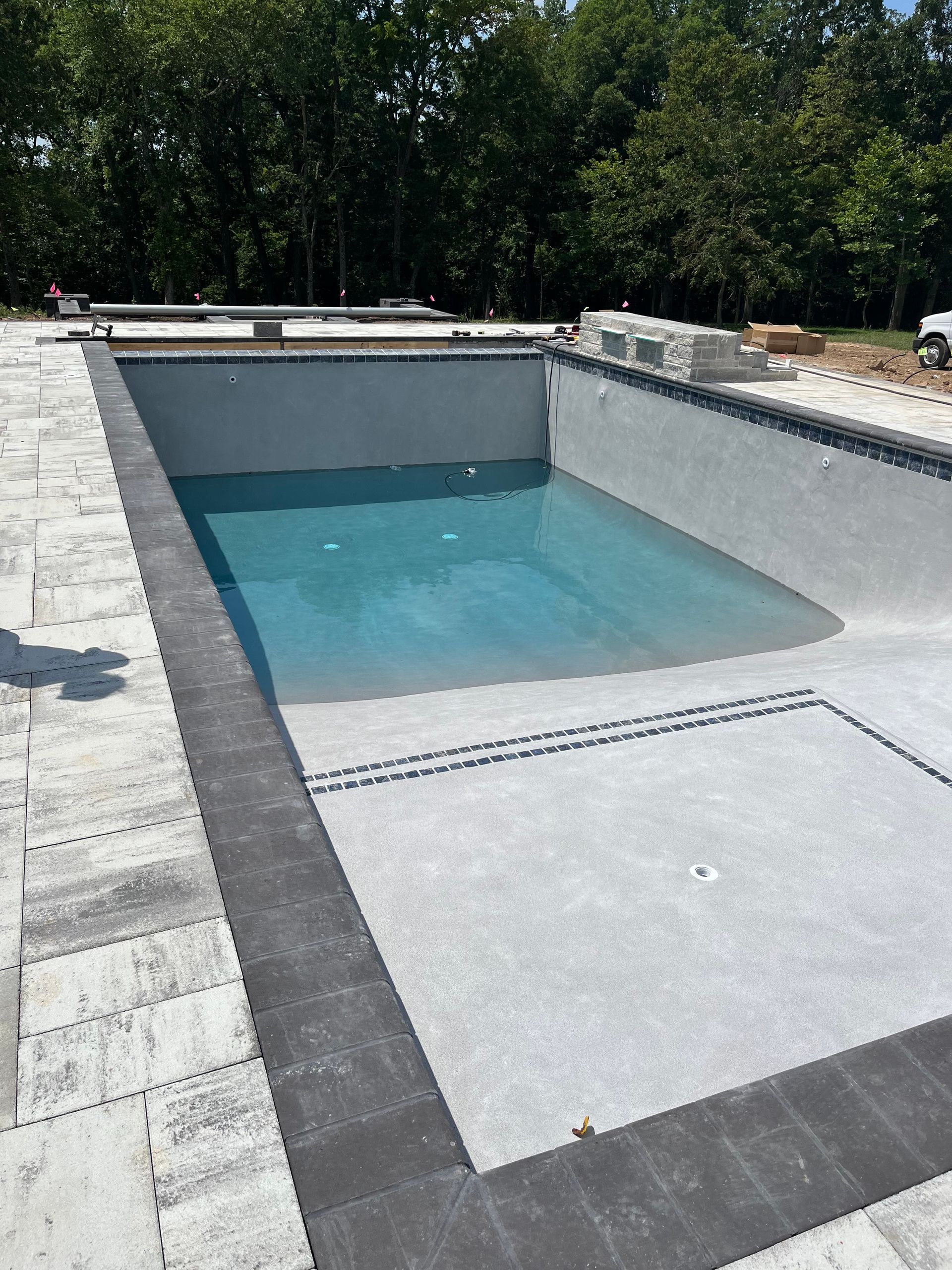 Rectangular in-ground swimming pool with gray concrete and a dark border. Water is clear blue.
