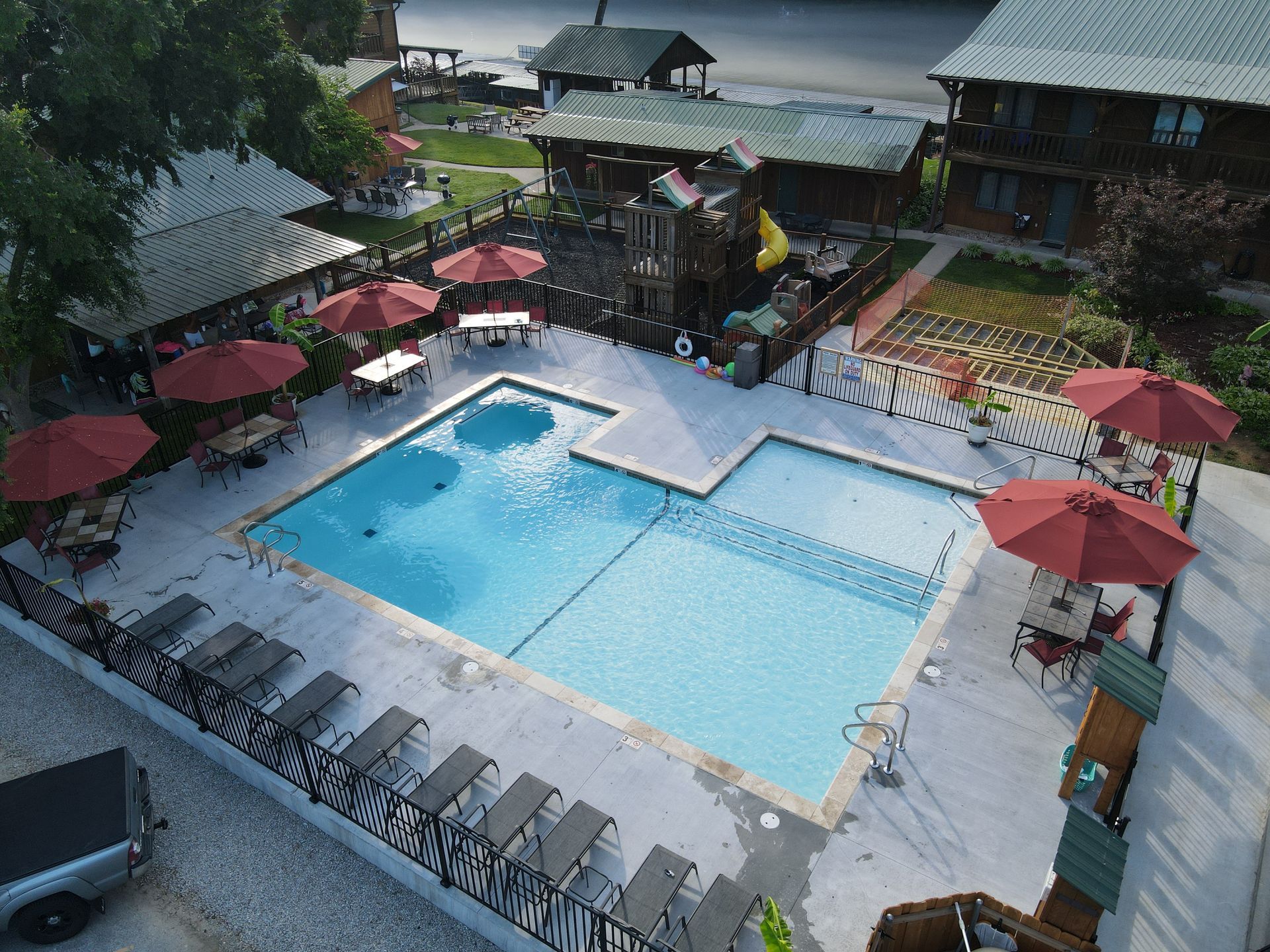 Swimming pool surrounded by buildings, red umbrellas, and lounge chairs.