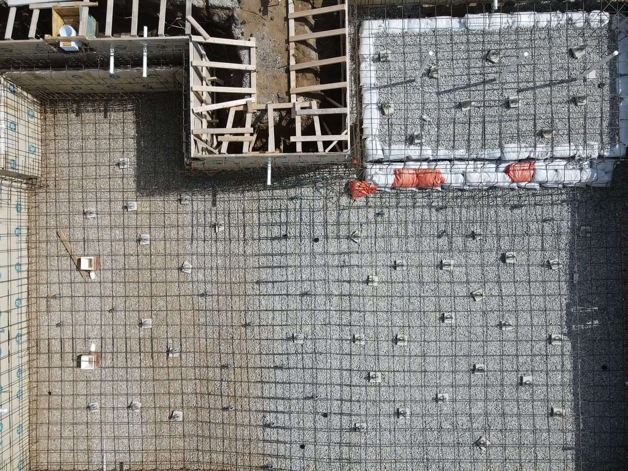 Overhead view of a construction site: Rebar grid laid out for concrete foundation, with wooden forms visible.