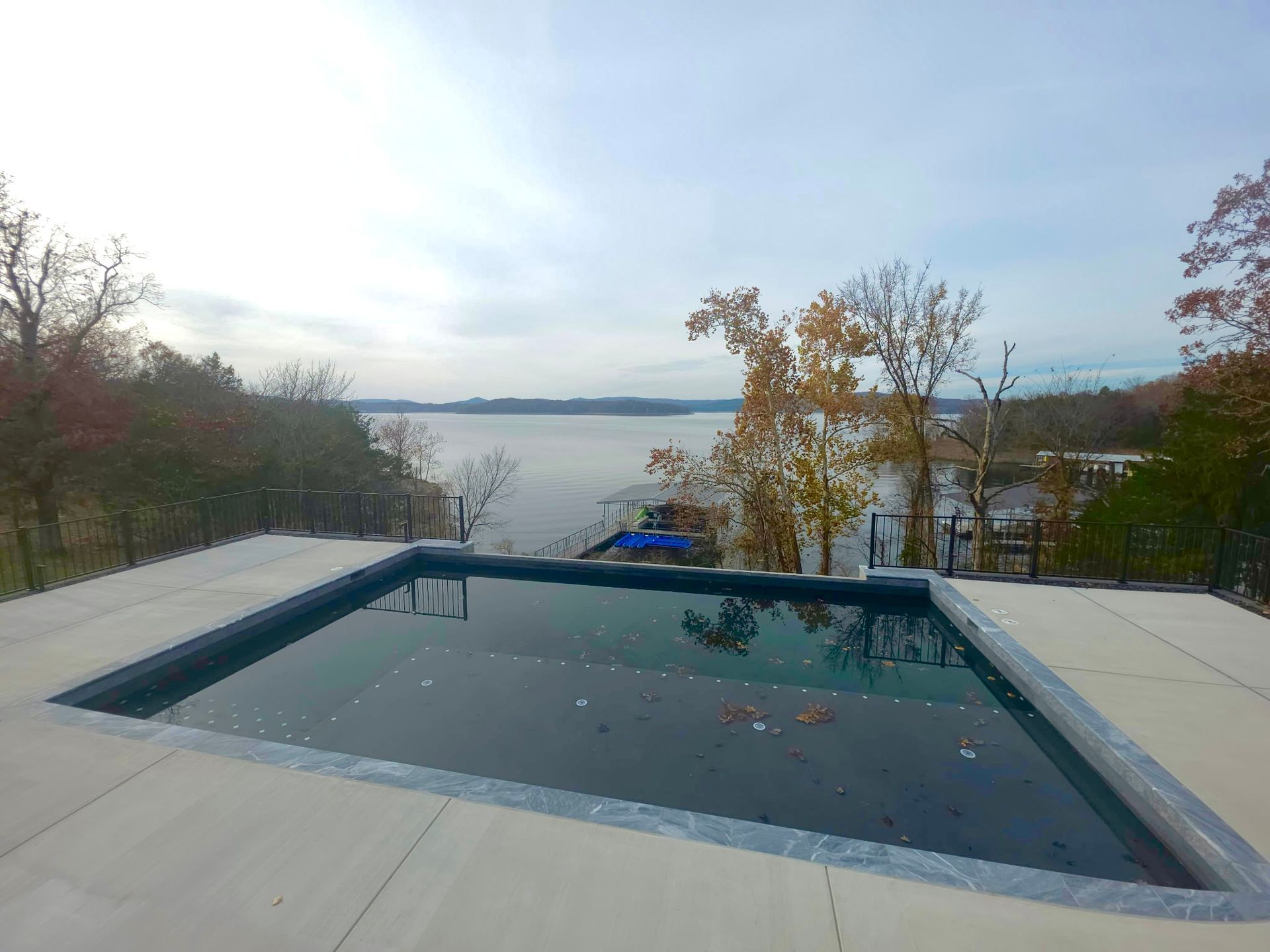 Swimming pool overlooking a lake on a cloudy day. Pool is rectangular with light concrete surround.