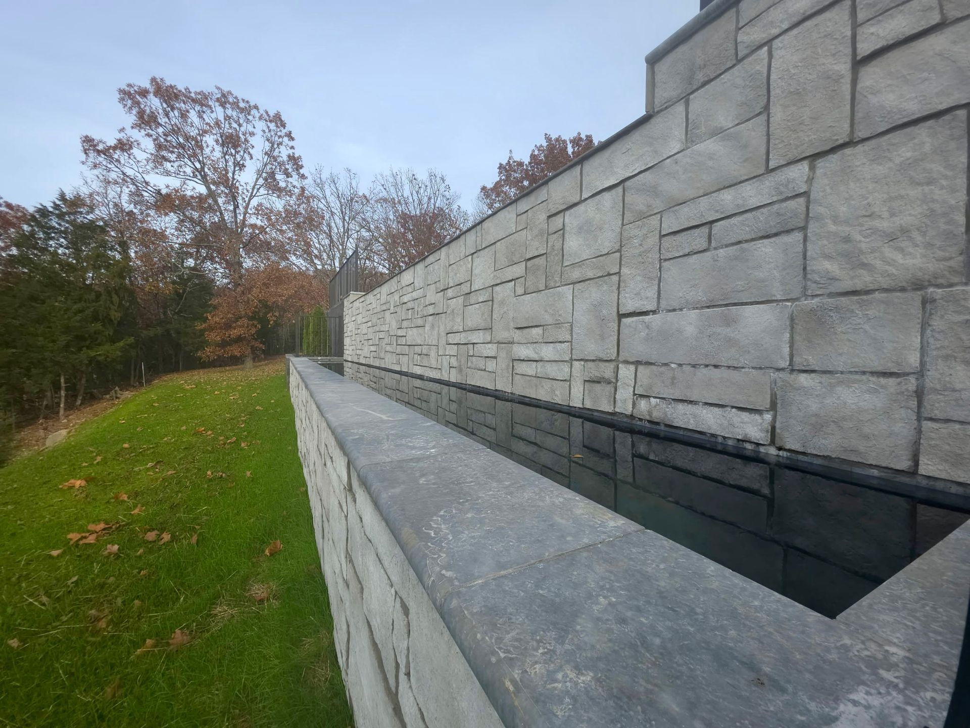 Stone wall with a reflecting pool and trees in the background.