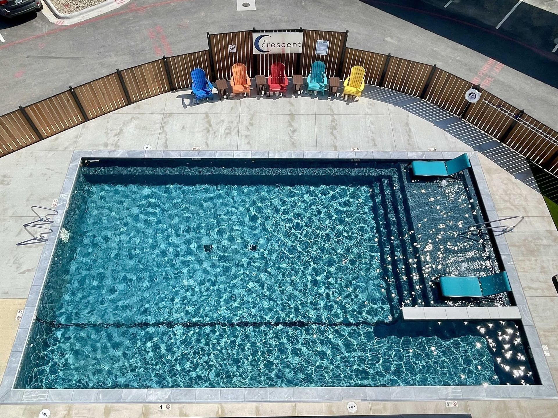 Pool with steps, lounge chairs, and colorful Adirondack chairs behind a fence.