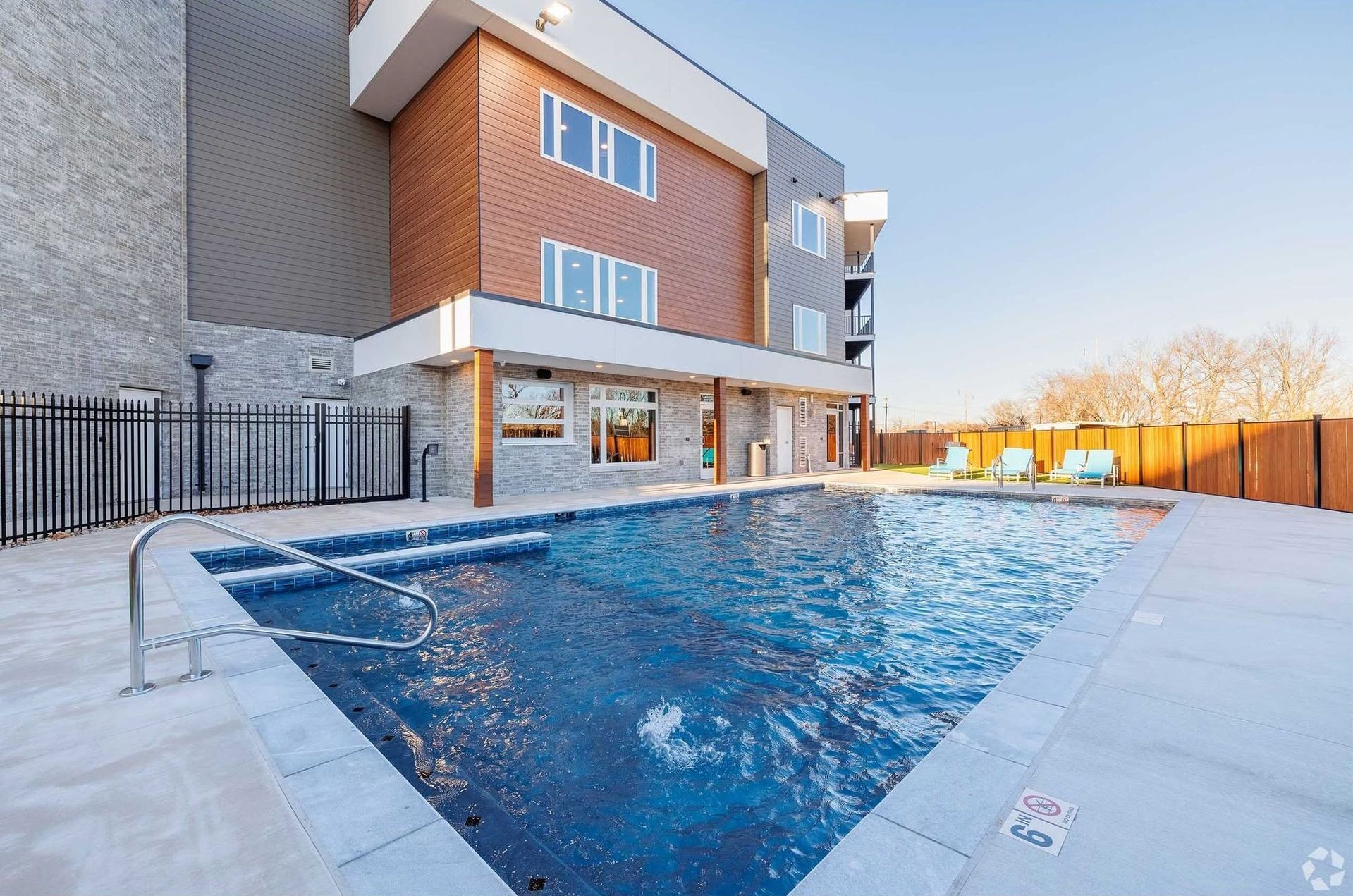 A rectangular outdoor swimming pool in front of a modern apartment building.