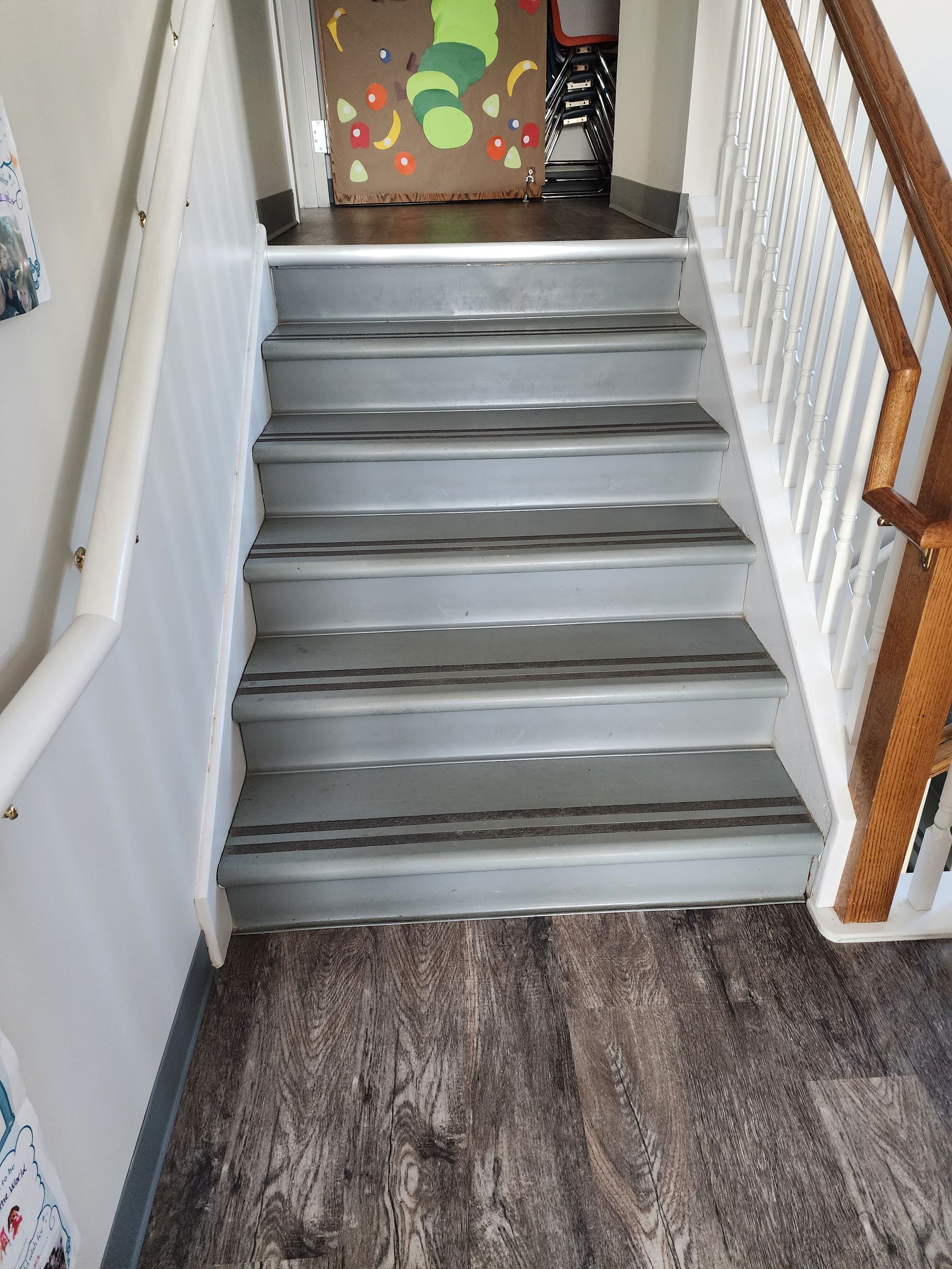 Gray staircase with a white railing on the left and a wood railing on the right, wooden floor.