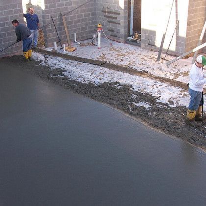 Workers smoothing concrete at a construction site beside a brick building.