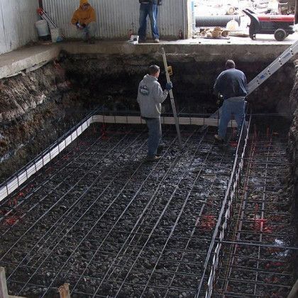 Workers preparing rebar in a deep concrete foundation pit at a construction site
