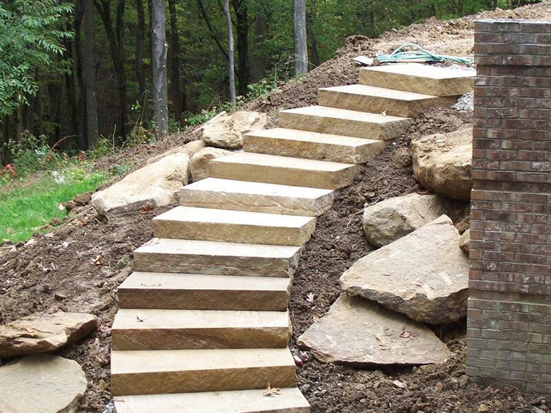 Curving stone steps built into a wooded hillside beside a brick wall