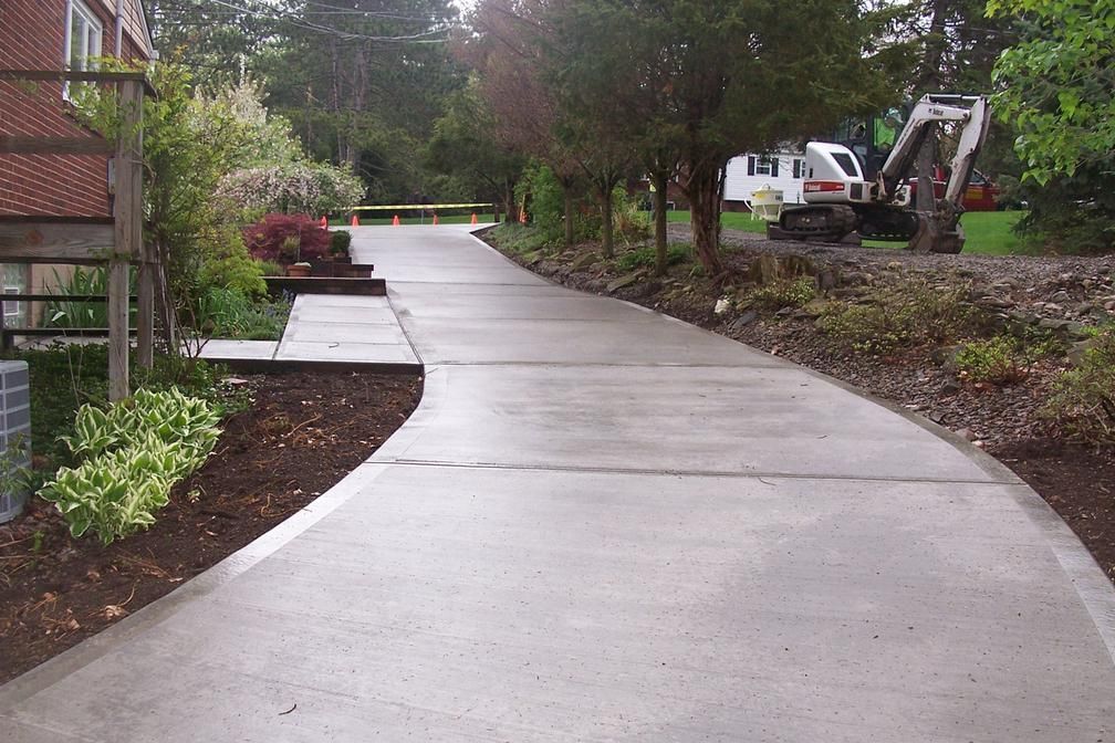 New concrete walkway curving through a landscaped residential area with trees and parked vehicles