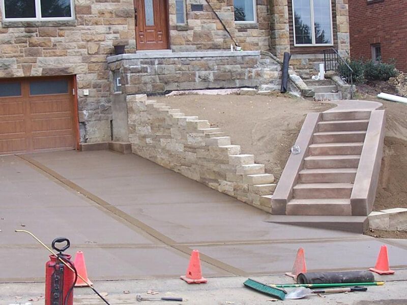 House driveway with stone retaining wall under construction, traffic cones, and steps leading to the entry.
