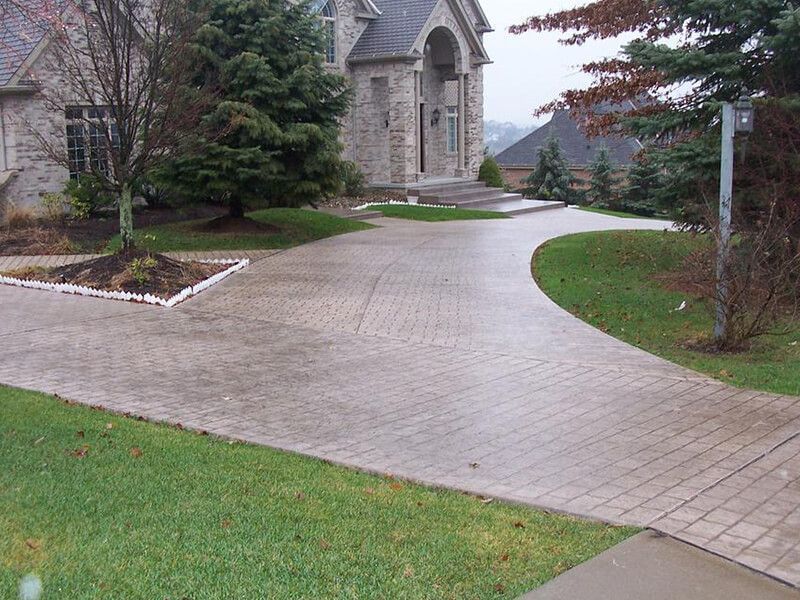 Stone house driveway curving past green lawns and trees on a quiet residential property