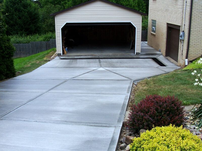 Concrete driveway leading to an open garage beside a house and landscaped yard