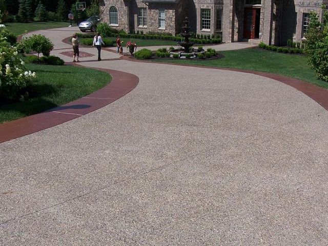 Curved gravel driveway bordered by red edging and green landscaping leading to a stone house