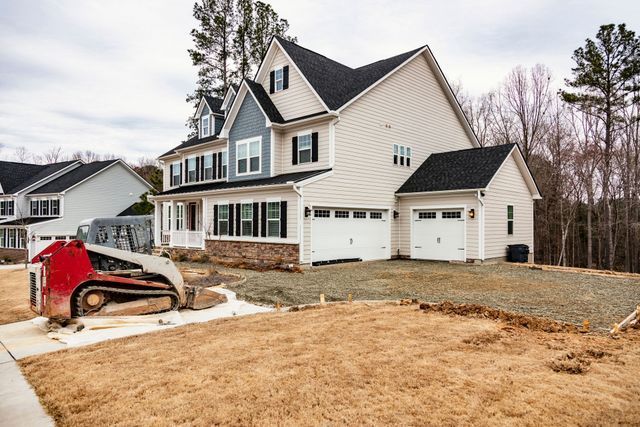 Large beige two-story house under construction with a Bobcat and unfinished yard at the front