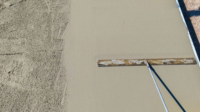 Close-up of wet concrete being smoothed beside rough gravel, with a trowel handle visible.