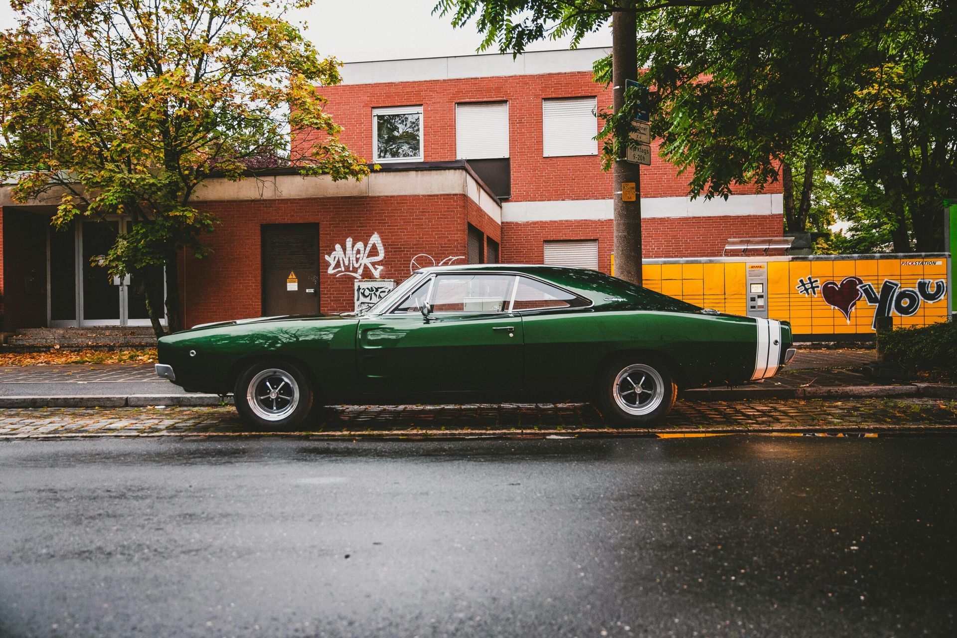 Green classic car parked on wet street; brick building in background.