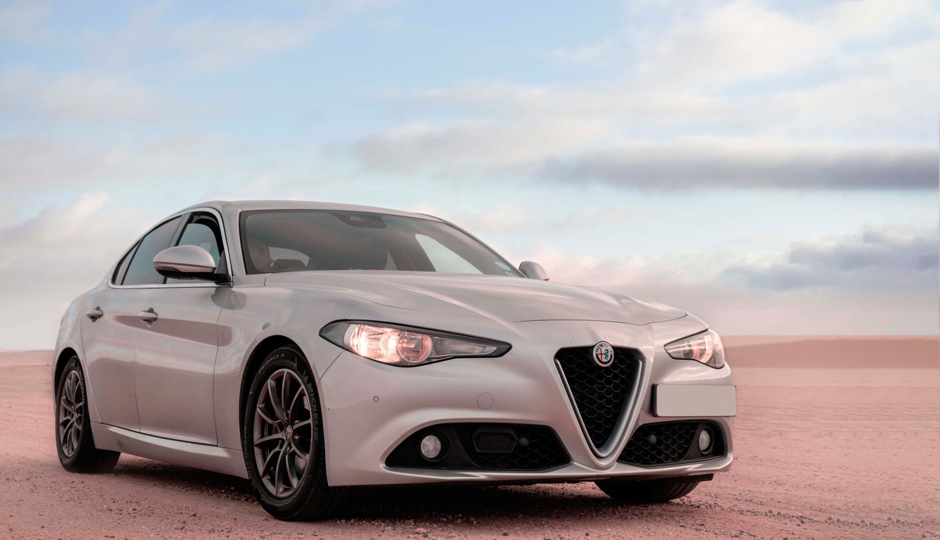 Silver Alfa Romeo Giulia sedan parked on a desert landscape, sky in background.