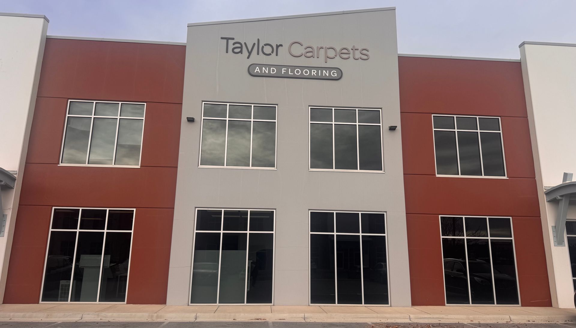 Taylor Carpets storefront with brown and gray facade, multiple windows, and a cloudy sky.