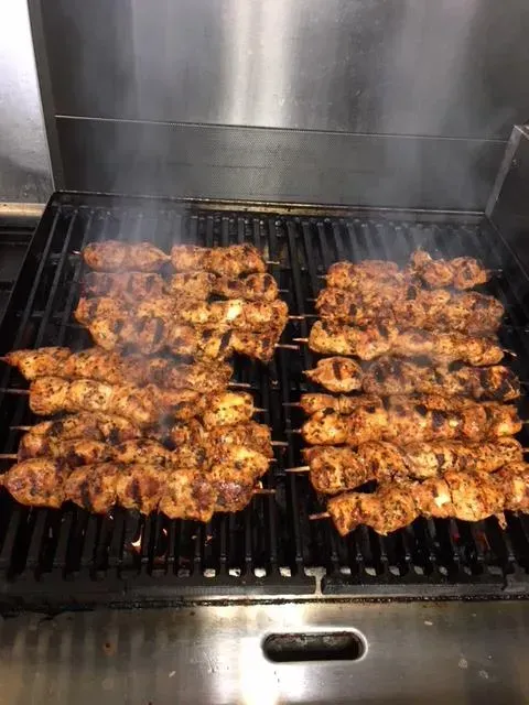 A bunch of chicken skewers are cooking on a grill.