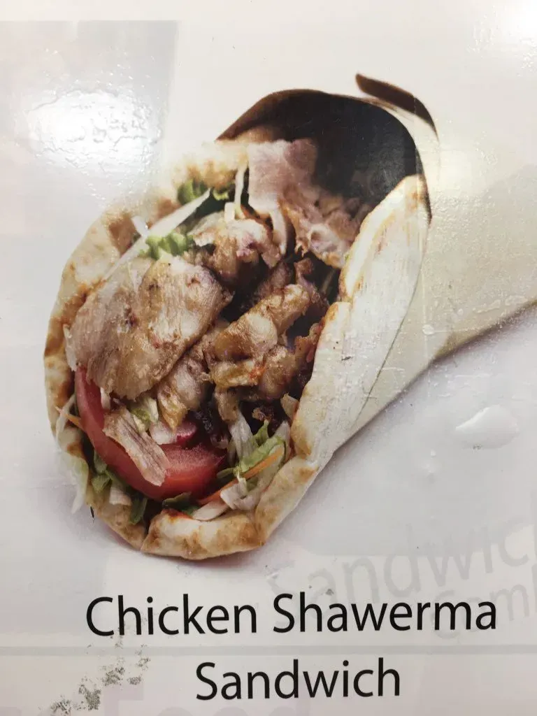 A close up of a chicken shawarma sandwich on a white surface.