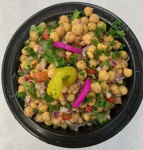 A black bowl filled with chickpeas , onions , peppers and other vegetables.