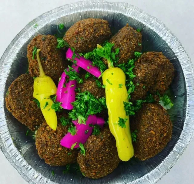 A tin foil container filled with falafel and peppers.