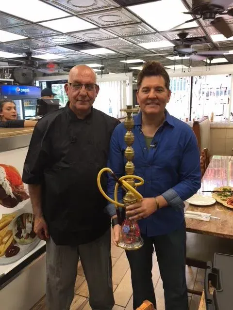 Two men are standing next to each other in a restaurant holding a hookah.