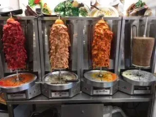 A row of shawarma grills filled with different types of meat and sauces.