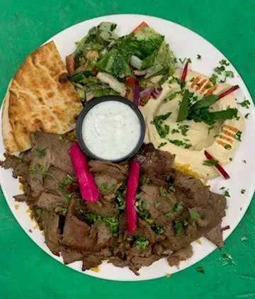 A plate of food with meat , vegetables and pita bread on a green table.