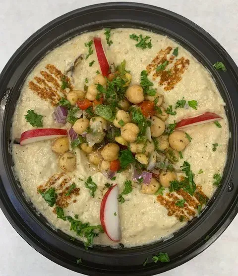 A close up of a bowl of hummus with chickpeas and radishes on a table.