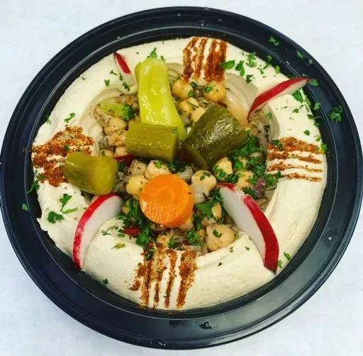 A bowl of hummus with chickpeas carrots and radishes.
