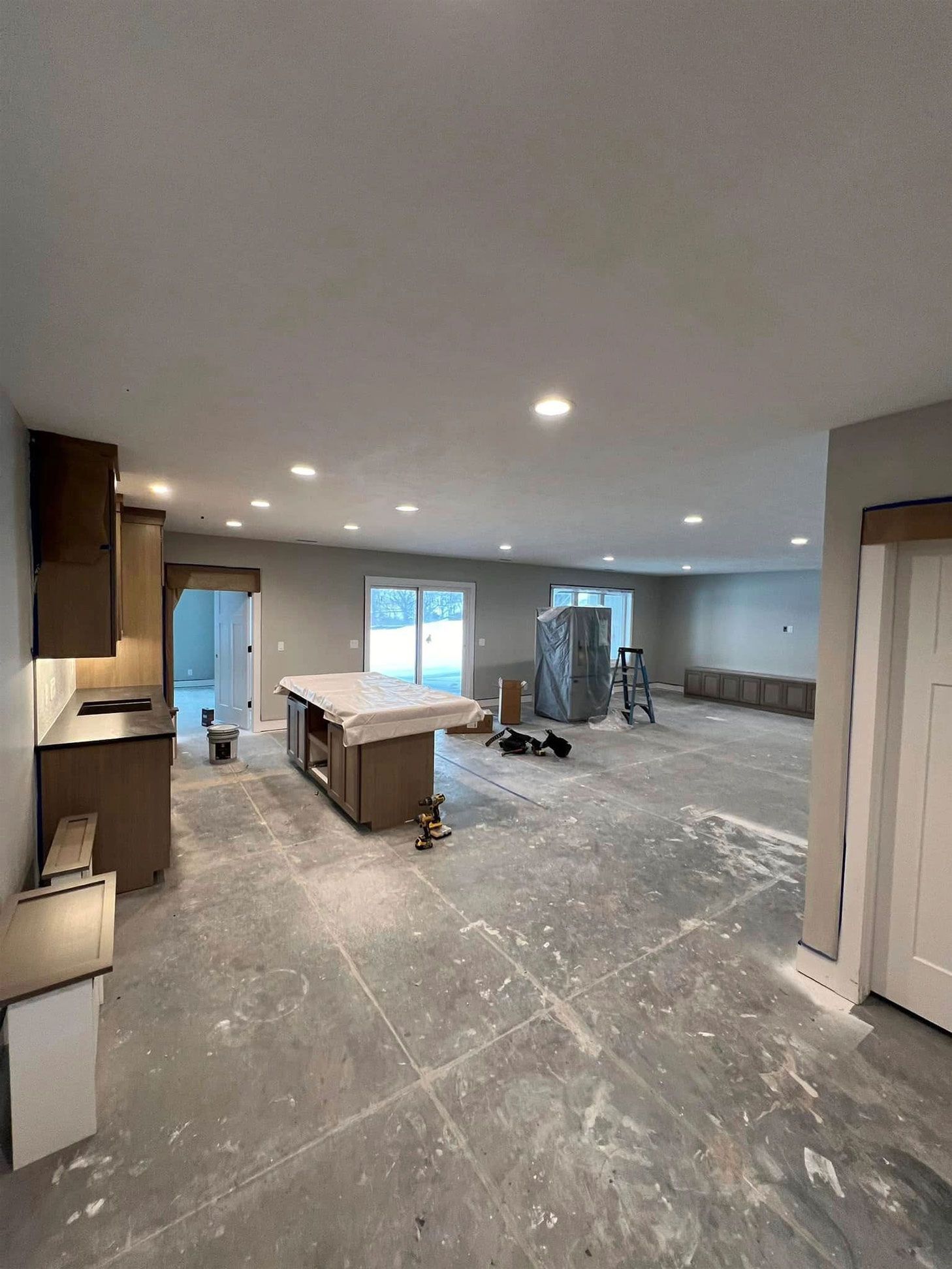 Empty, unfinished kitchen with cabinets, island, sliding glass doors, and recessed lighting.