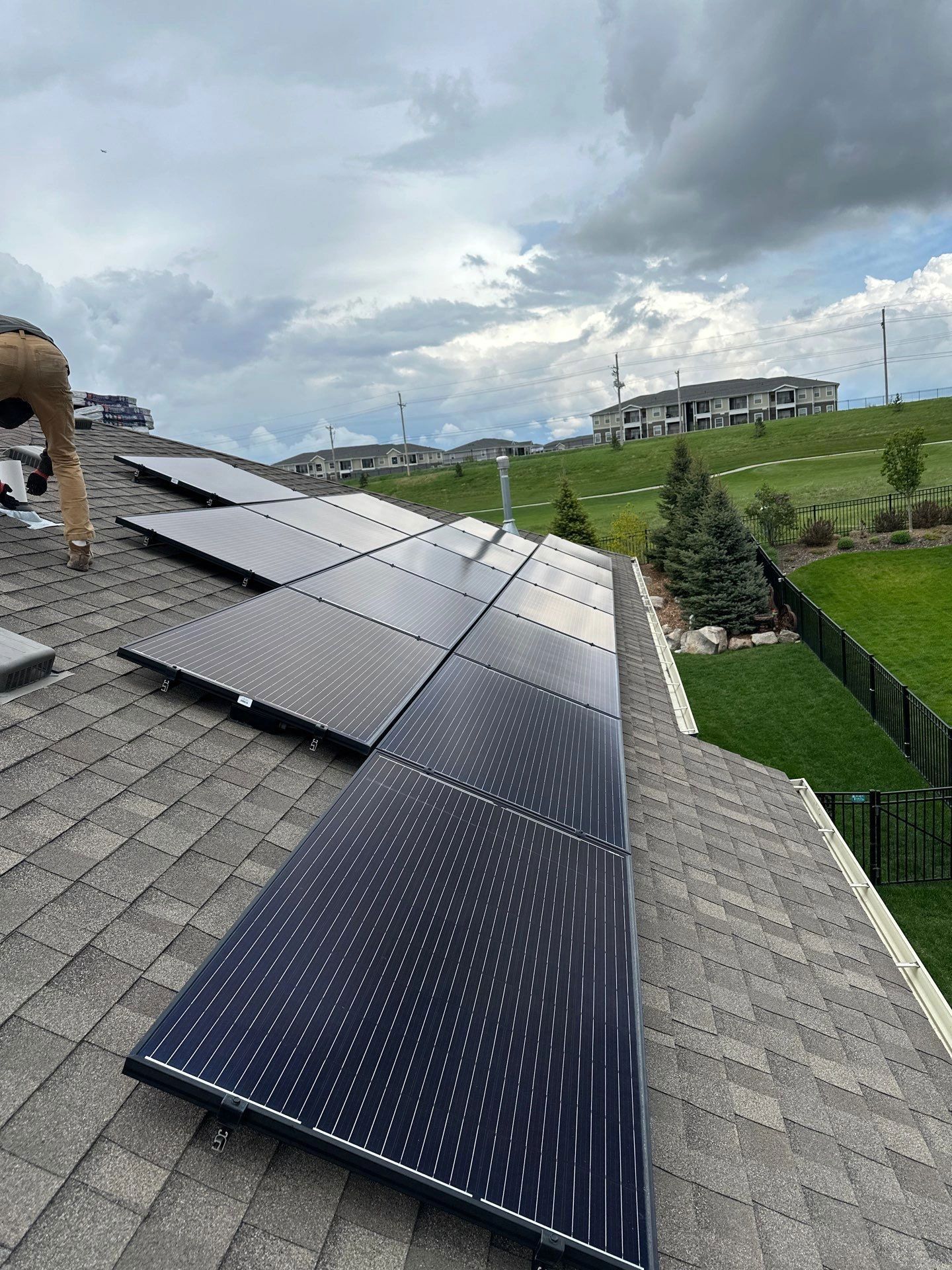 Solar panels installed on a residential roof with a worker nearby, against a cloudy sky.