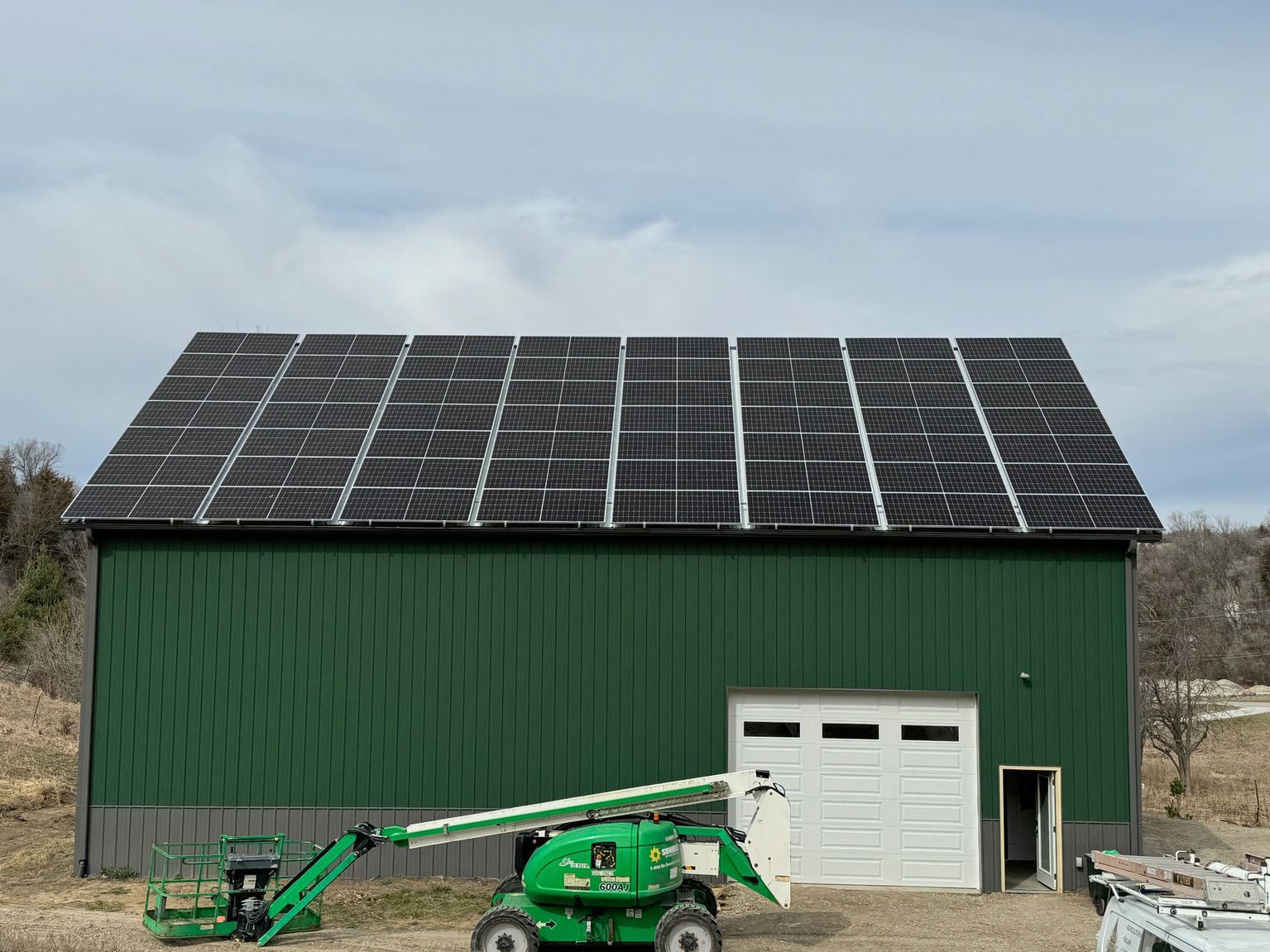 Green barn with solar panels on the roof and a lift in front of a closed garage door.