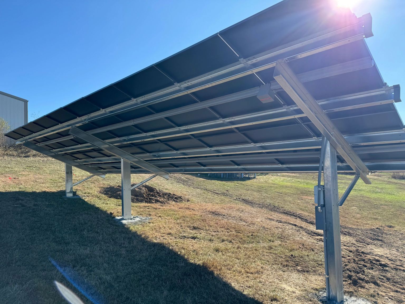 Solar panels mounted on metal supports on a grassy hill, bright sun in the upper right.