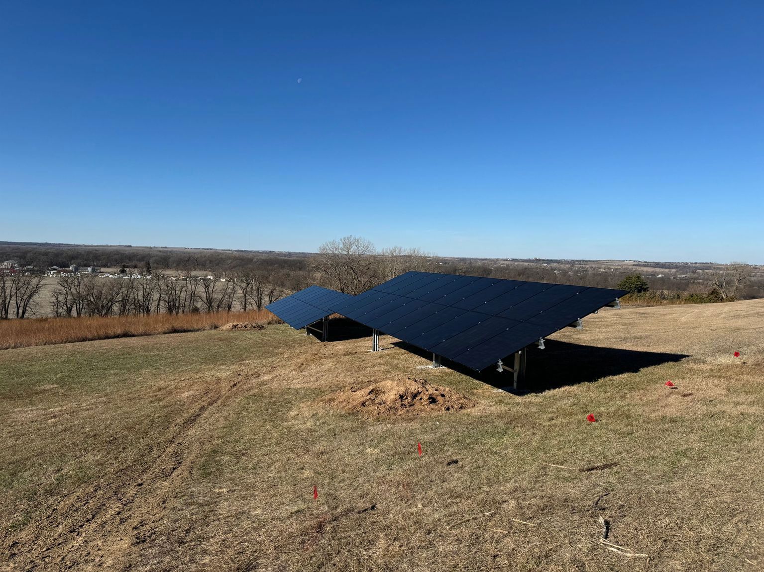 Solar panels on a grassy hill under a bright blue sky, with a distant town visible.