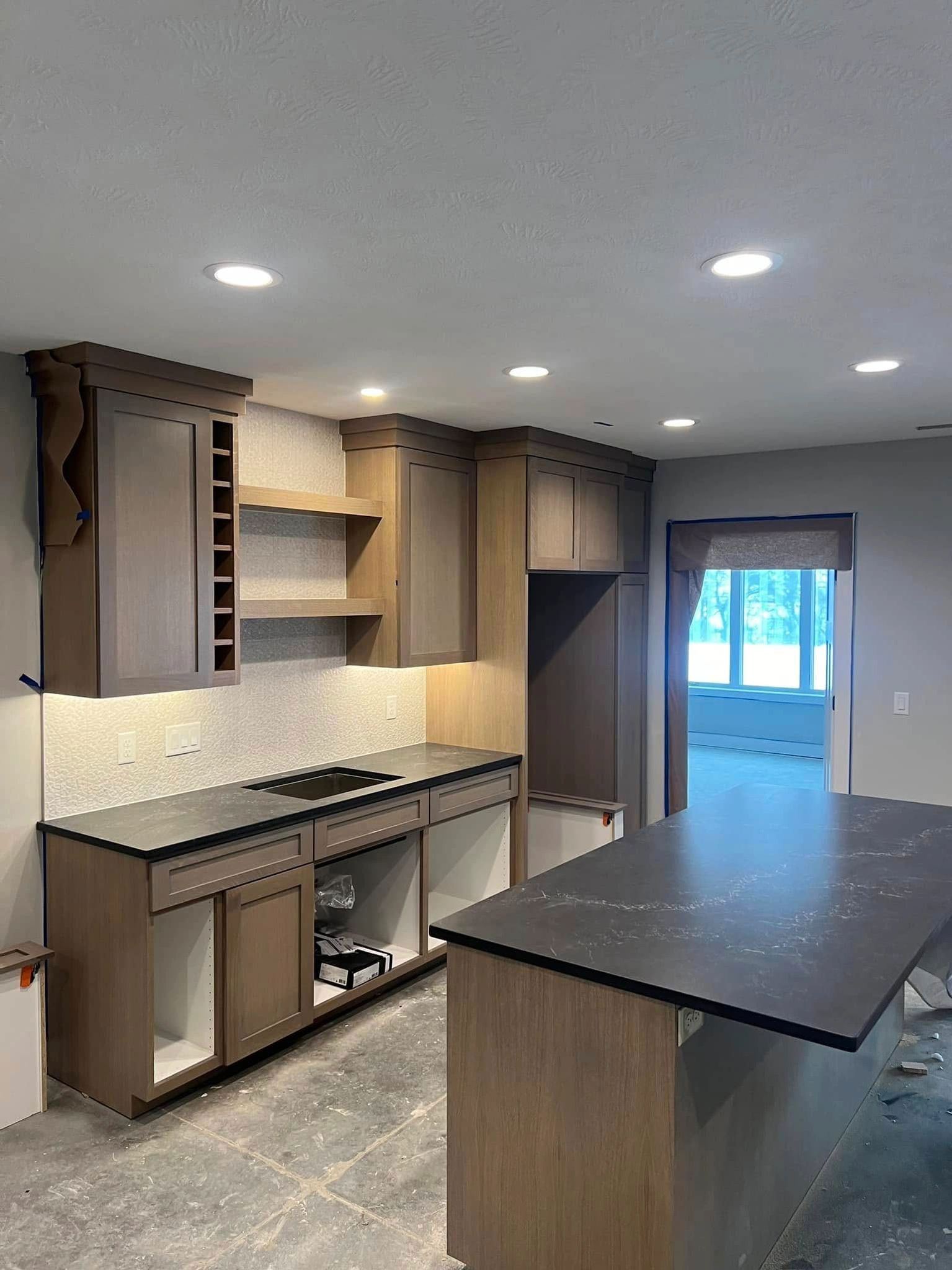 Kitchen under construction with gray cabinets, black countertops, and island.