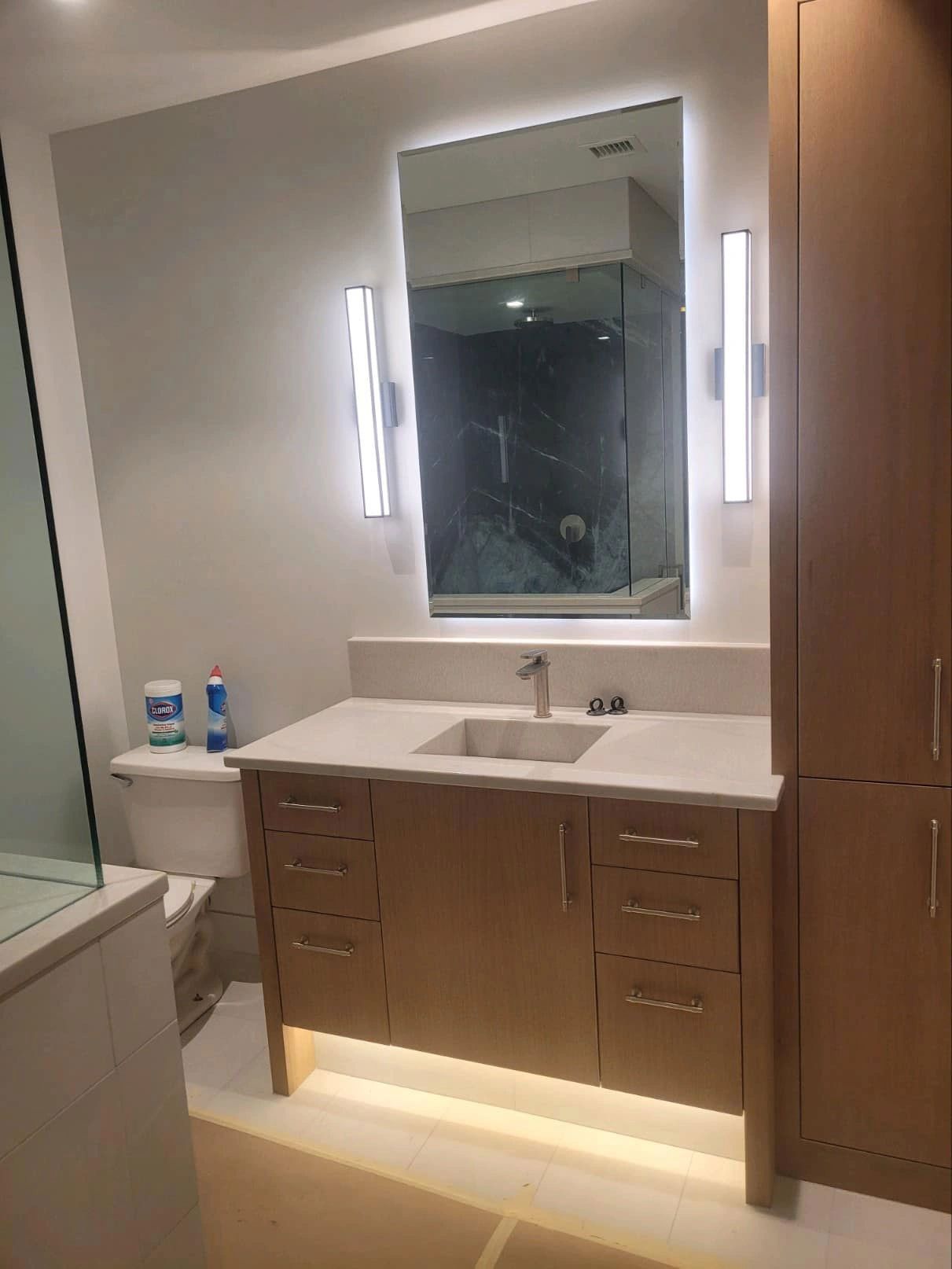 Bathroom with light wood vanity, illuminated mirror, and tall cabinet.