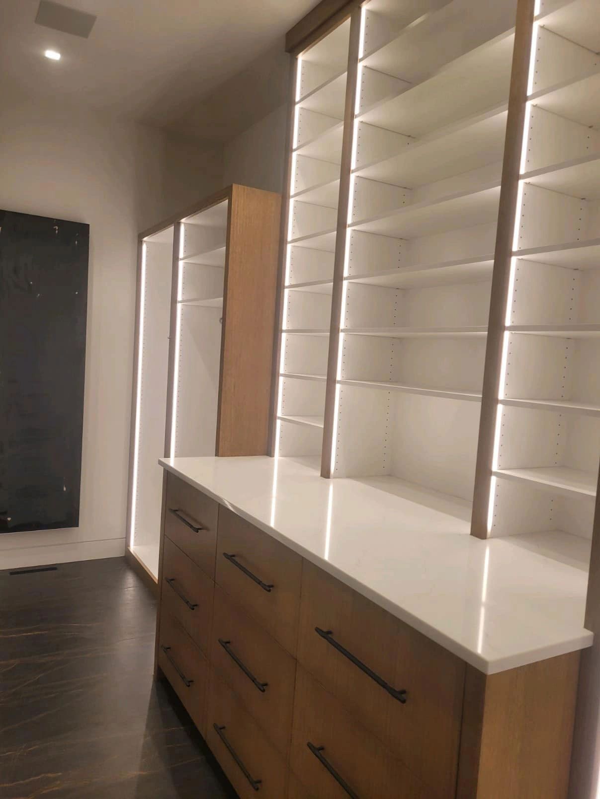 Built-in closet with white shelves, LED lighting, and wooden drawers; white countertop. Dark wood floor.