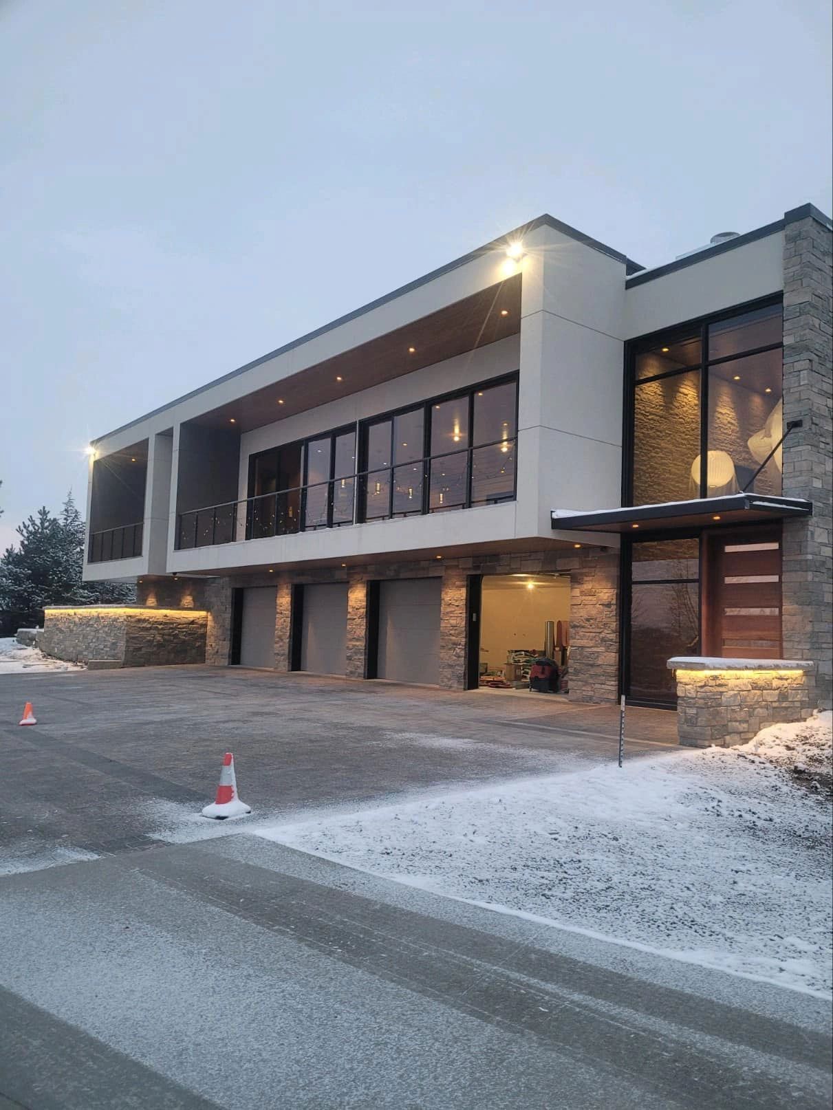 Modern two-story house with stone and white facade, large windows, and garage doors. Snow on the ground.