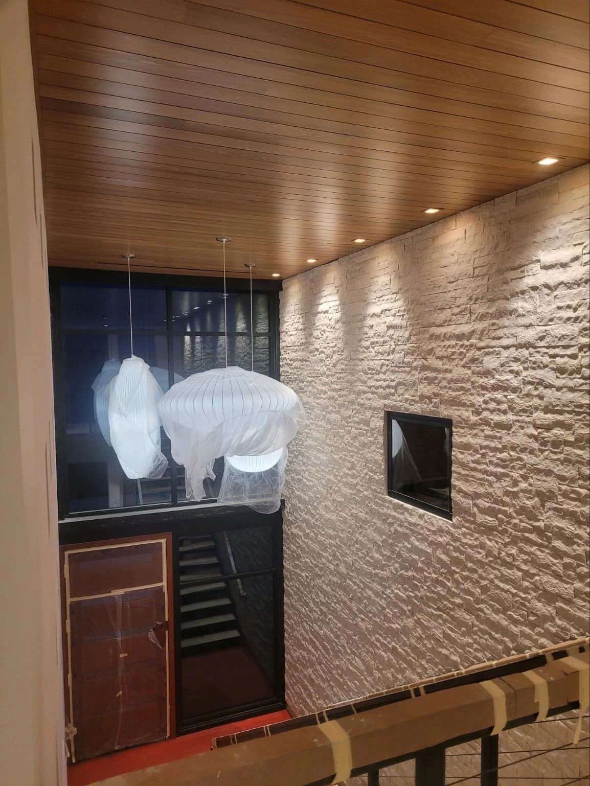 Interior view of a building with stone wall, wood ceiling, stairs, and a dark doorway.