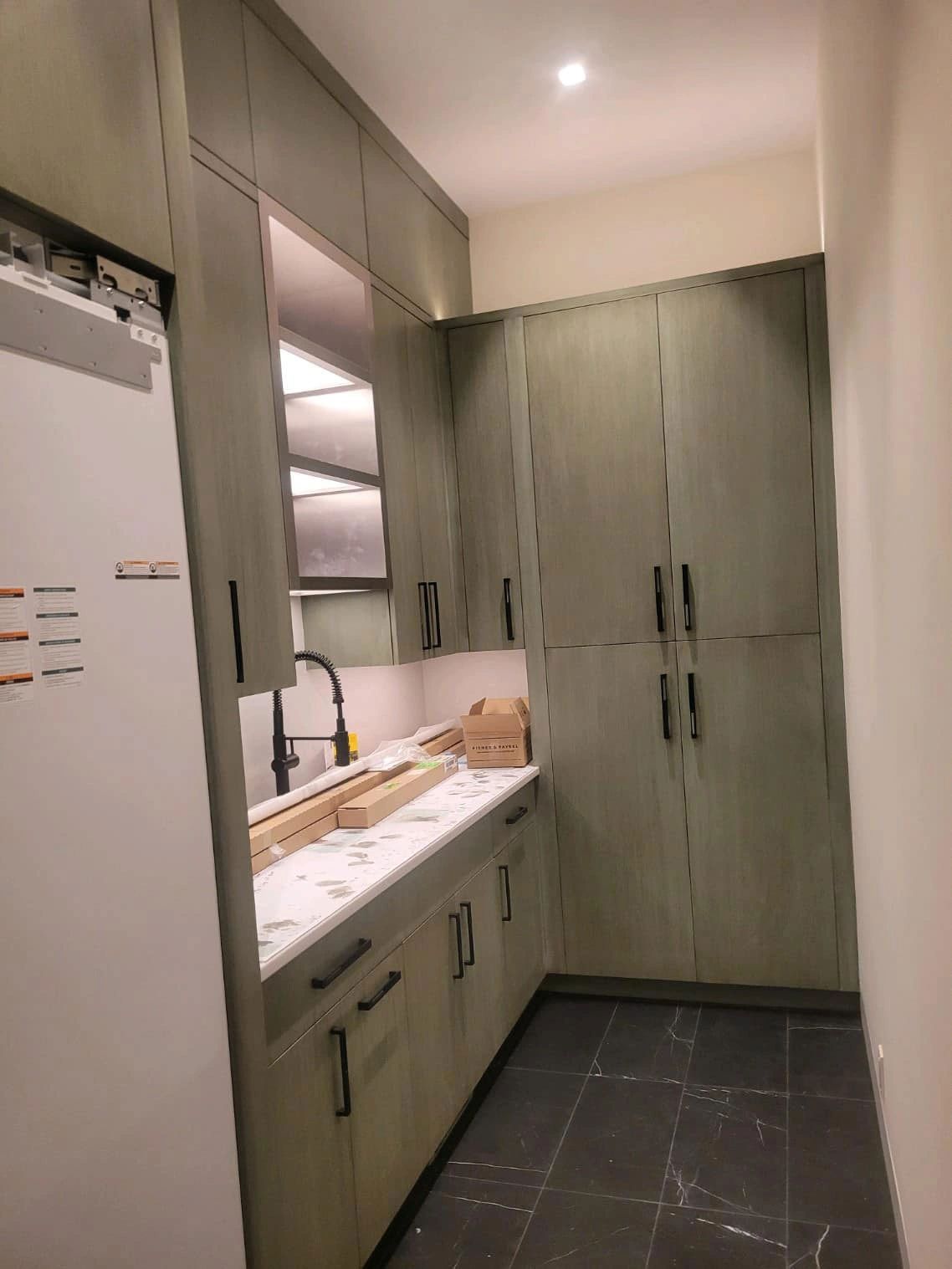 A kitchen with light green cabinets, marble countertop, black hardware, and dark tile floor.